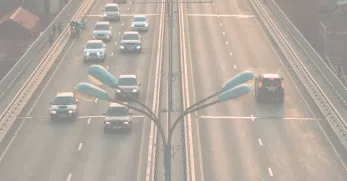 An overhead view of cars traveling on a multilane highway with streetlights in the middle, showing the systems of urban infrastructure.